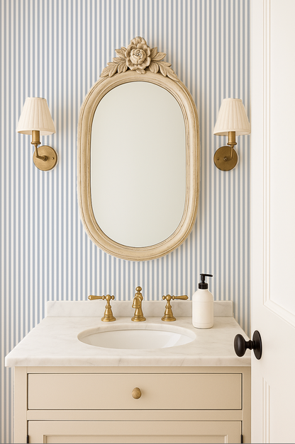 Bathroom with blue grey striped wallpaper, vintage mirror, and brass fixtures.
